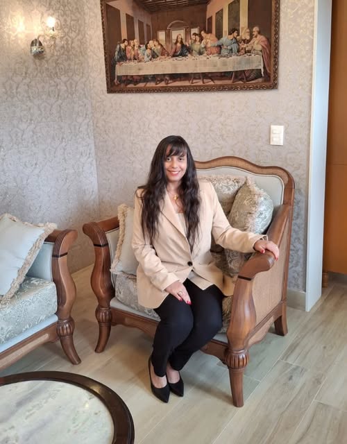 Rebeca Andrade sentada em uma poltrona clássica de madeira, em ambiente com papel de parede adamascado